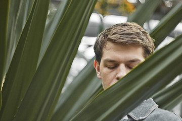 Handsome man in depression. Not shaved hipster in a botanical garden, holding on to his head. Concept: headache and grief.