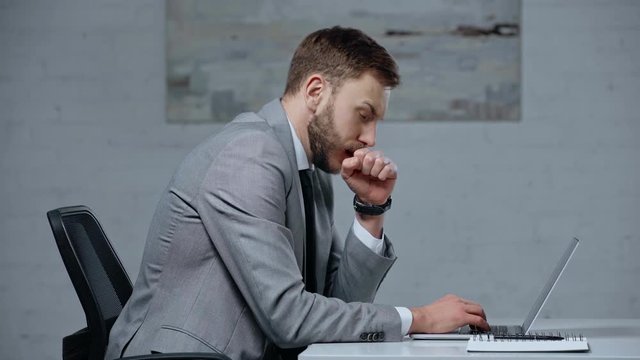 diseased businessman coughing while typing on laptop