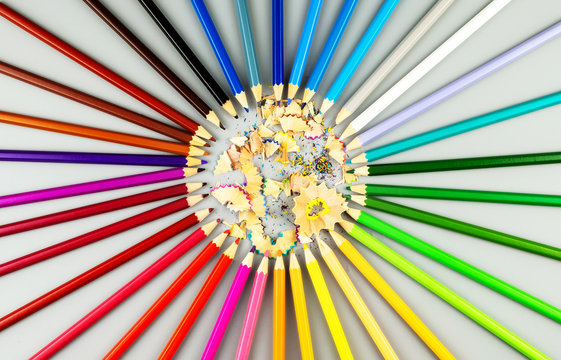 Multicolored pencils are arranged in a circle shape with wooden chips in the center
