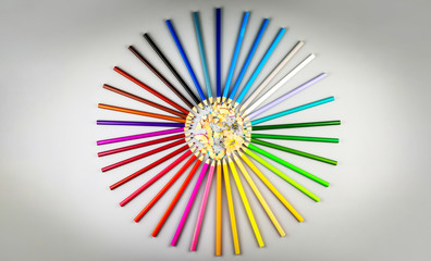 Multicolored pencils are arranged in a circle shape with wooden chips in the center