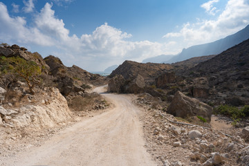 empty curved road in mountains with rocks, blue sky and few clouds, off road, desert