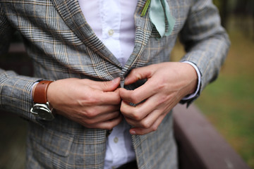 Young handsome stylish man dressed in modern formal clothes buttoning jacket. Close up of hands of guy in gray jacket, violet shirt. Person ready for wedding celebration or graduation.
