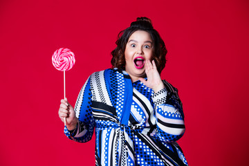 Plus size model with wide open mouth holding big lollipop on red background