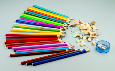 Multicolored pencils with sharpening and chips on a gray background