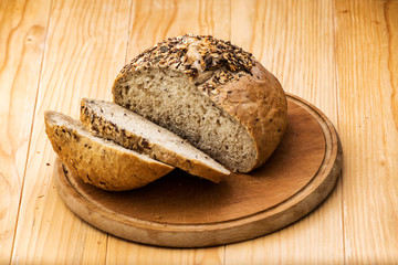 Loaf of wheat bread sprinkled with various seeds, with a cut slices of bread on a wooden table