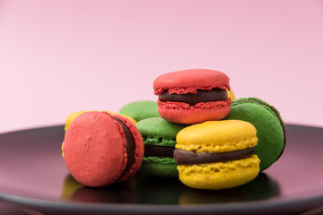 Close Up View of Tasty french macarons in a black plate on pink pastel background. Red, yellow and green macarons