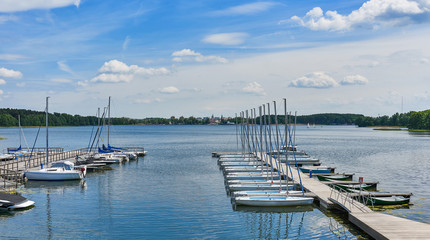 Beautiful landscape presenting sailboats and motorboats moored to the pier in the bay of the lake in the port against the background of clouds and blue sky on a sunny day in Olsztyn Warmia and Mazury