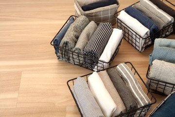 Vertical tidying up storage. Neatly folded clothes neutral colors in the metal black baskets for wardrobe. Wooden background. Nordic style.