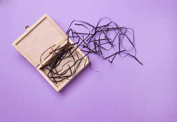 open wood box with black filler lying on purple background, top view