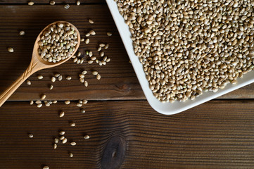 hemp seeds in a ceramic plate and rustic wooden spoon on dark wooden background. flat lay.