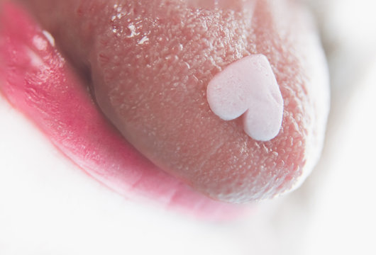 Heart shaped pil on tongue in macro close-up. Party drug.