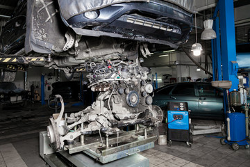 Replacement used engine on a table mounted under raised car on lift  for installation after a breakdown and repair in a vehicle workshop as a guarantee for the dealership. Auto service industry.