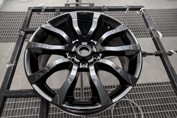 A black painted aluminum alloy wheel is mounted on a special frame during drying in a chamber in a...