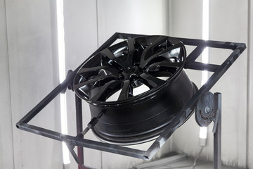 A black painted aluminum alloy wheel is mounted on a special frame during drying in a chamber in a...