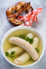 Bavarian snack with boiled white sausages in bouillon and a pretzel, vertical shot on a beige stone background