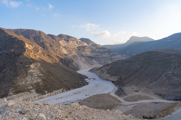 Panorama of a mountain range and a valley in Oman, dry landscape with mountains, rocks, stones and sand, sunny weather with some clouds