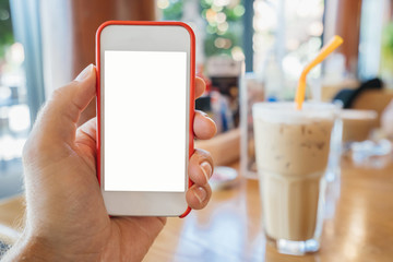 The mock-up of a samrtphone in a man’s hand is white in a red frame, against the background of a cafe and a cold drink of coffee lat, summer, day.