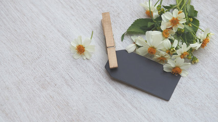 Blank black color card and blooming flowers on white color rustic wood table for business and holiday background concepts