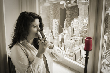 Frau trinkt einen Kaffee und schaut nachdenklich aus dem Fenster auf new york Woman drinks Caffee and looks down on the city of new york