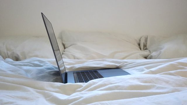 Laptop on a bed with a crumpled white sheet.