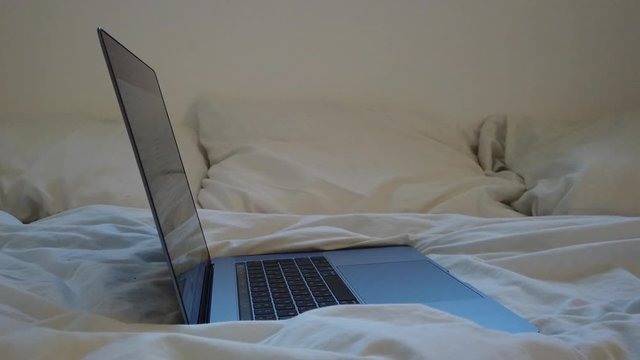 Laptop on a bed with a crumpled white sheet.