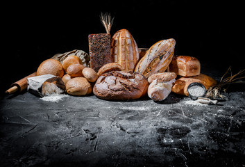 Assortment of fresh baked bread on dark background. White and rye bread, buns with copy place