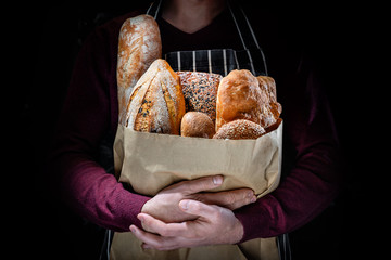 A man in an apron holds many kinds of freshly baked bread