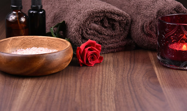 Romantic spa and wellness still life with red rose stock images. Spa and wellness setting. Red rose, bath salt, brown towels, cosmetic phials and candle on a wooden background with copy space for text