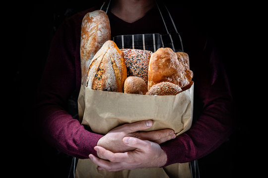 A man in an apron holds many kinds of freshly baked bread