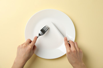 Female hands hold fork and knife on beige background with plate, top view