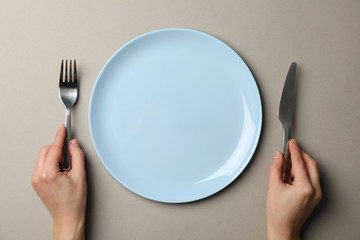 Female hands hold fork and knife on grey craft background with plate, top view