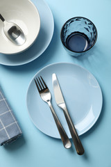 Tableware and cutlery on blue background, top view