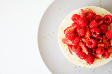 French dessert. Lime mousse cake with lime biscuit and red berries filling. Cake decorated with fresh berries and a lime zest. Cake is on a light grey plate, on a light background. 