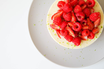 French dessert. Lime mousse cake with lime biscuit and red berries filling. Cake decorated with fresh berries and a lime zest. Cake is on a light grey plate, on a light background. 
