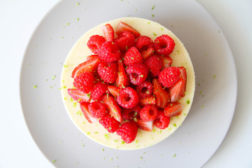 French dessert. Lime mousse cake with lime biscuit and red berries filling. Cake decorated with fresh berries and a lime zest. Cake is on a light grey plate, on a light background. 