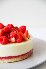 French dessert. Lime mousse cake with lime biscuit and red berries filling. Cake decorated with fresh berries and a lime zest. Cake is on a light grey plate, on a light background. 