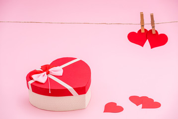 Heart shaped gift box and red paper hearts on pink pastel background. Clothes pegs and red paper hearts on rope. Valentines day concept