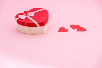 Heart shaped gift box and red paper hearts on pink pastel background. Valentines day concept