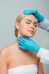 cropped view of beautician in blue latex gloves touching woman with closed eyes and plastic surgery...
