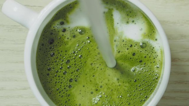 Pouring milk into green matcha tea, slow motion