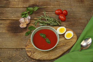 gazpacho spanish tomato soup topped with basil and tomatoes and garlic and egg on wooden rustic background. Top view. Copy space. Concept of national cuisine