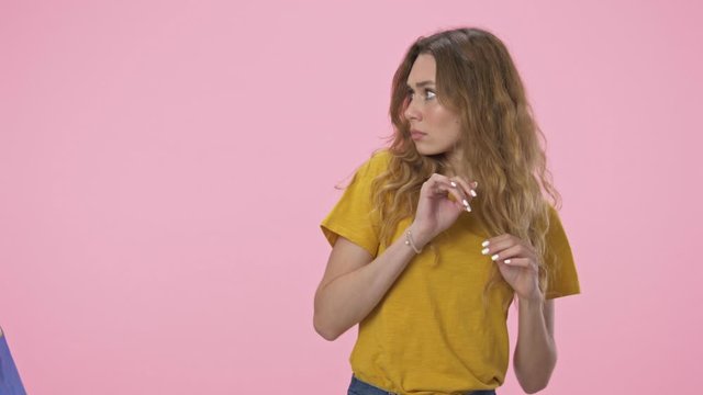 A pretty young woman pushes away a string bags with plastic waste isolated over pink background