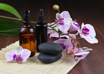 Fototapeta na wymiar Spa and wellness setting with purple orchid stock images. Black massage stones with pink orchid and cosmetic phials stock images. Spa-concept with zen stonesand purple orchid flower