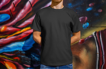 Mockup black male t-shirt on a young guy against the background of a wall with graffiti, front view.