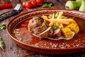 Baked pork served with french fries, corn and pesto, restaurant platter, Horizontal orientation