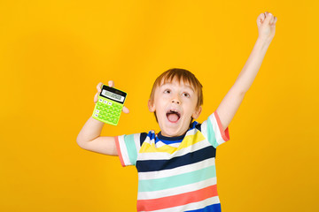 Cute little boy screaming yes, over yellow background. Kid using calculator. Child learning to count