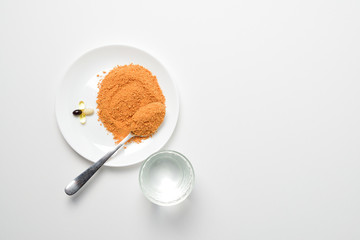 Tomato protein soup powder on a spoon. Meal replacement. Dry soup. Multivitamins, astaxanthin, fish oil, omega pills on a plate.  Closeup.