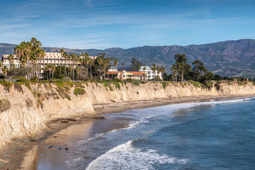 Goleta, CA, USA - January 2, 2020: UCSB, University California Santa Barbara. East side beige cliffs in front of several buildings. Blue ocean in front. Green foliage around. Hills on horizon and blue - obrazy, fototapety, plakaty