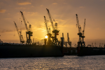 Obraz premium Hamburg, Germany. Cranes silhouetted against the evening sky in the harbor at dusk. The Port of Hamburg (German: Hamburger Hafen) is a sea port on the river Elbe. It is Germany's largest harbor.