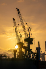 Obraz premium Hamburg, Germany. Cranes silhouetted against the evening sky in the harbor at dusk. The Port of Hamburg (German: Hamburger Hafen) is a sea port on the river Elbe. It is Germany's largest harbor.